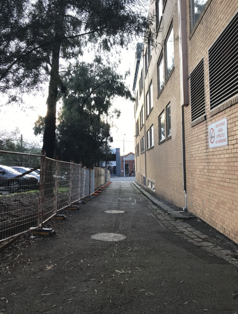 Image Description: A photograph of Dowling Place laneway showing a bitumen surface that is slightly uneven in some areas. This photo is taken from the front door at MESS, looking out onto the laneway towards Wreckyn Street. Image ends. 
